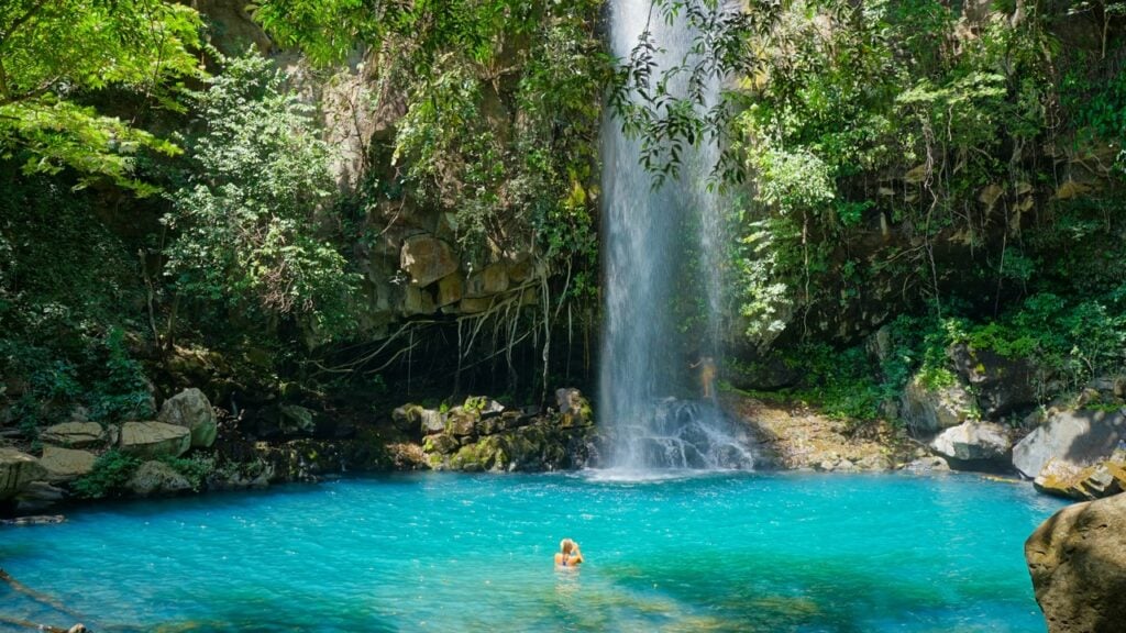 A beautiful waterfall in Costa Rica with one woman swimming in the waters.