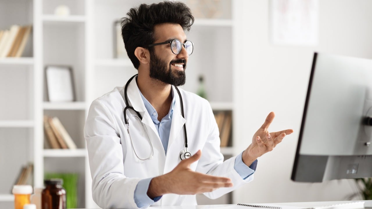 A young doctor on a video call with someone at his desk.