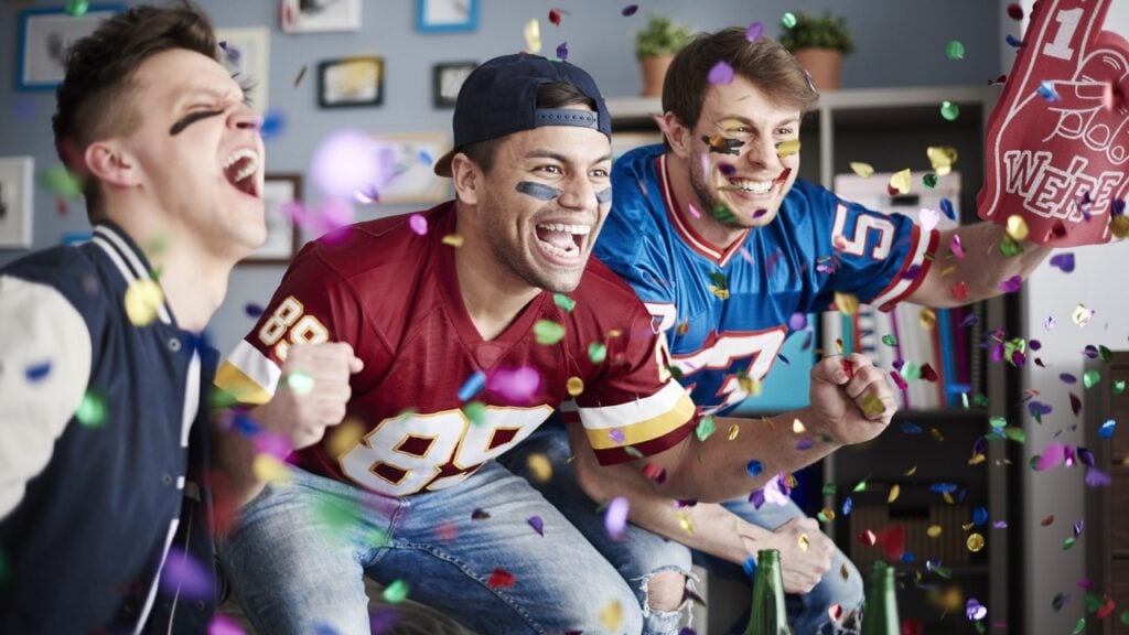 A group of men watching a sports game in a house and they're happy because their team won.