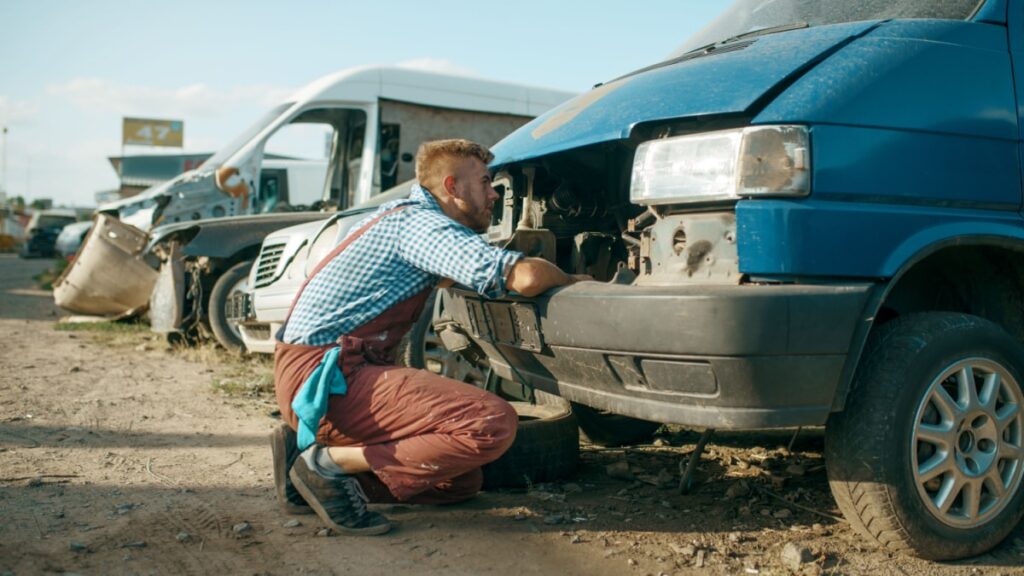 sell my junk car without title - Mechanic stuck head under the hood, car junkyard