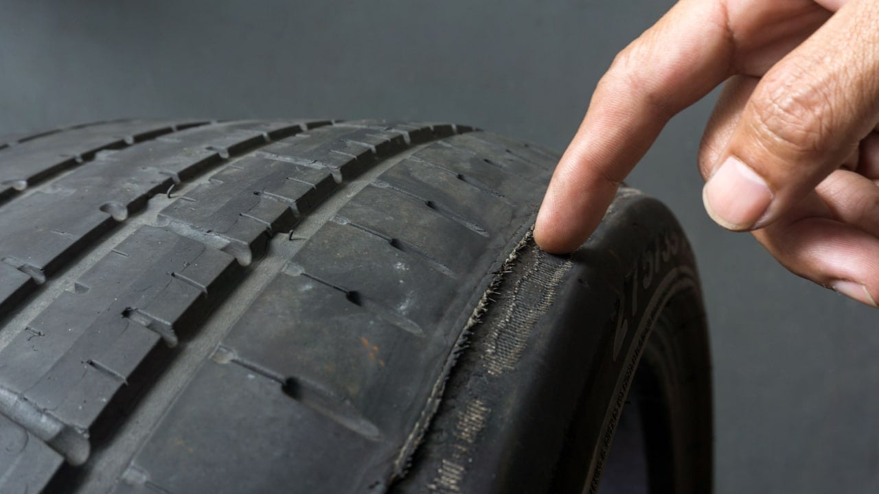 Finger pointing to damage on tire tread. Tire tread problems by tire pressure improper, Wheel alignment