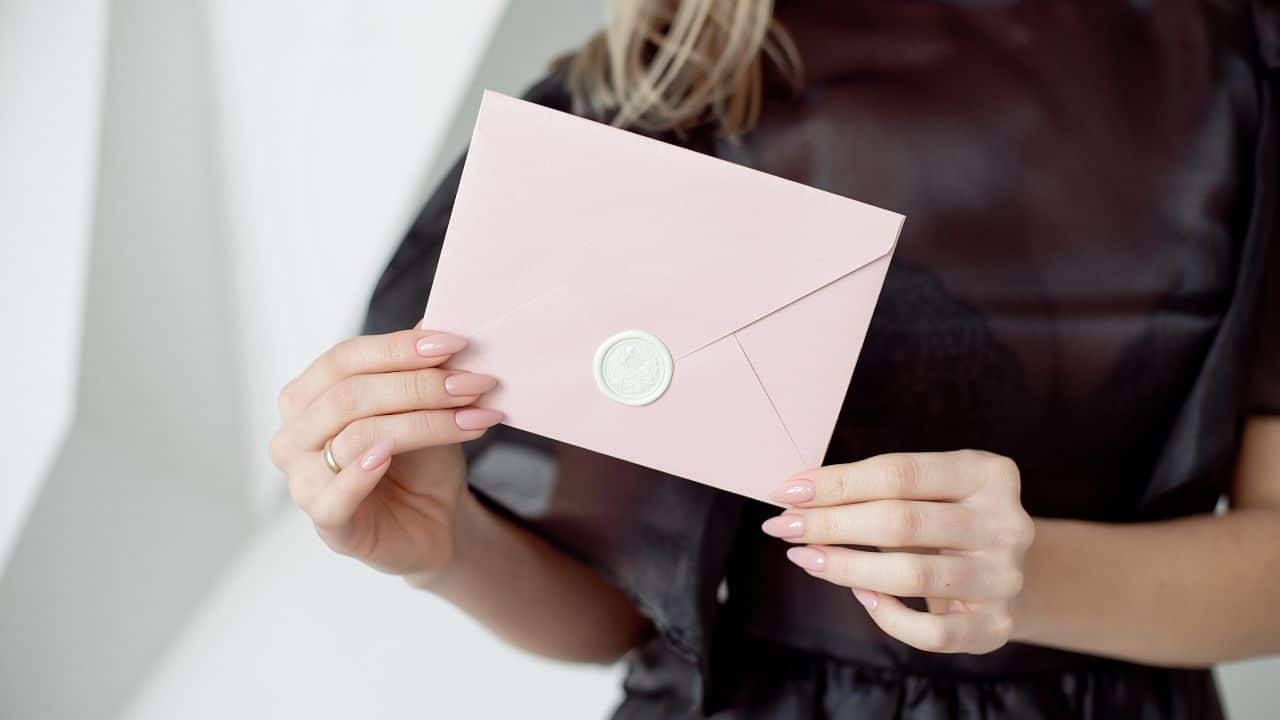 close-up photo of a female hands holding a pink invitation envelope with a wax seal, a gift certificate, a card, a wedding invitation card, writing a letter