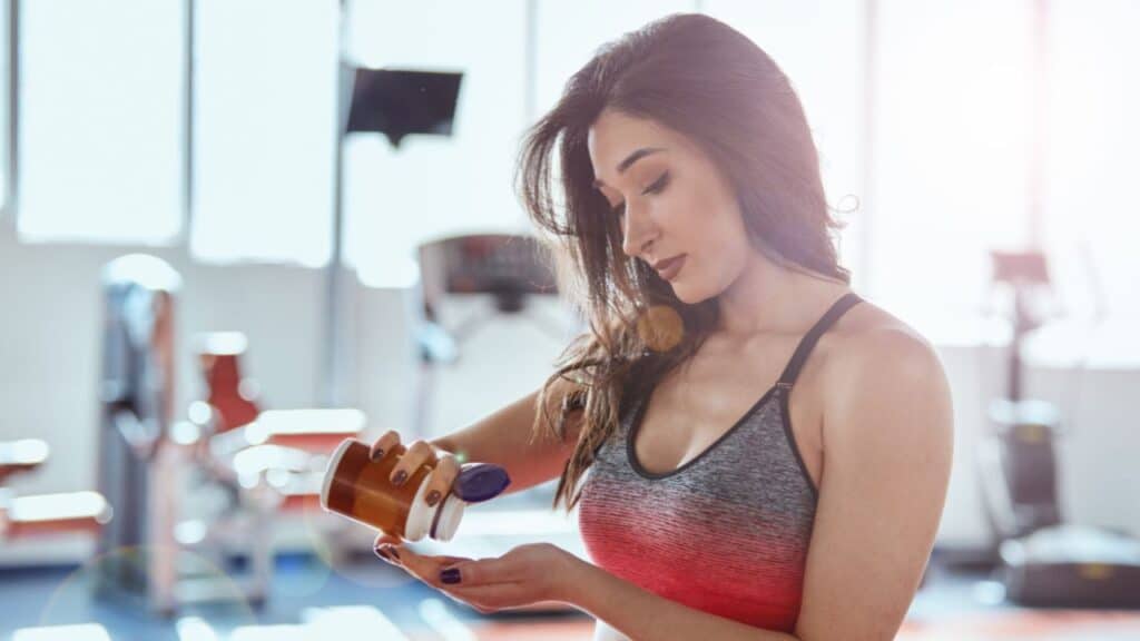 A fit sportswoman standing in a gym and taking pre workout pills, gym supplements