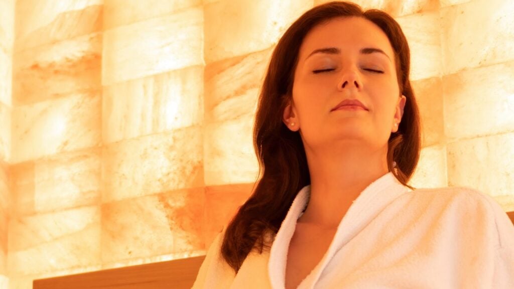 Himalayan salt blocks. Warm sauna with walls made of medicinal pink salt blocks. Prevention of the respiratory system diseases. A beautiful woman in a white robe is getting healthier in a salt cave.